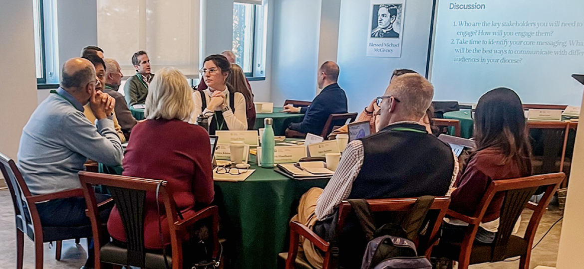 People seated around a conference table during a discussion, with a projection screen showing 'Discussion' in the room.