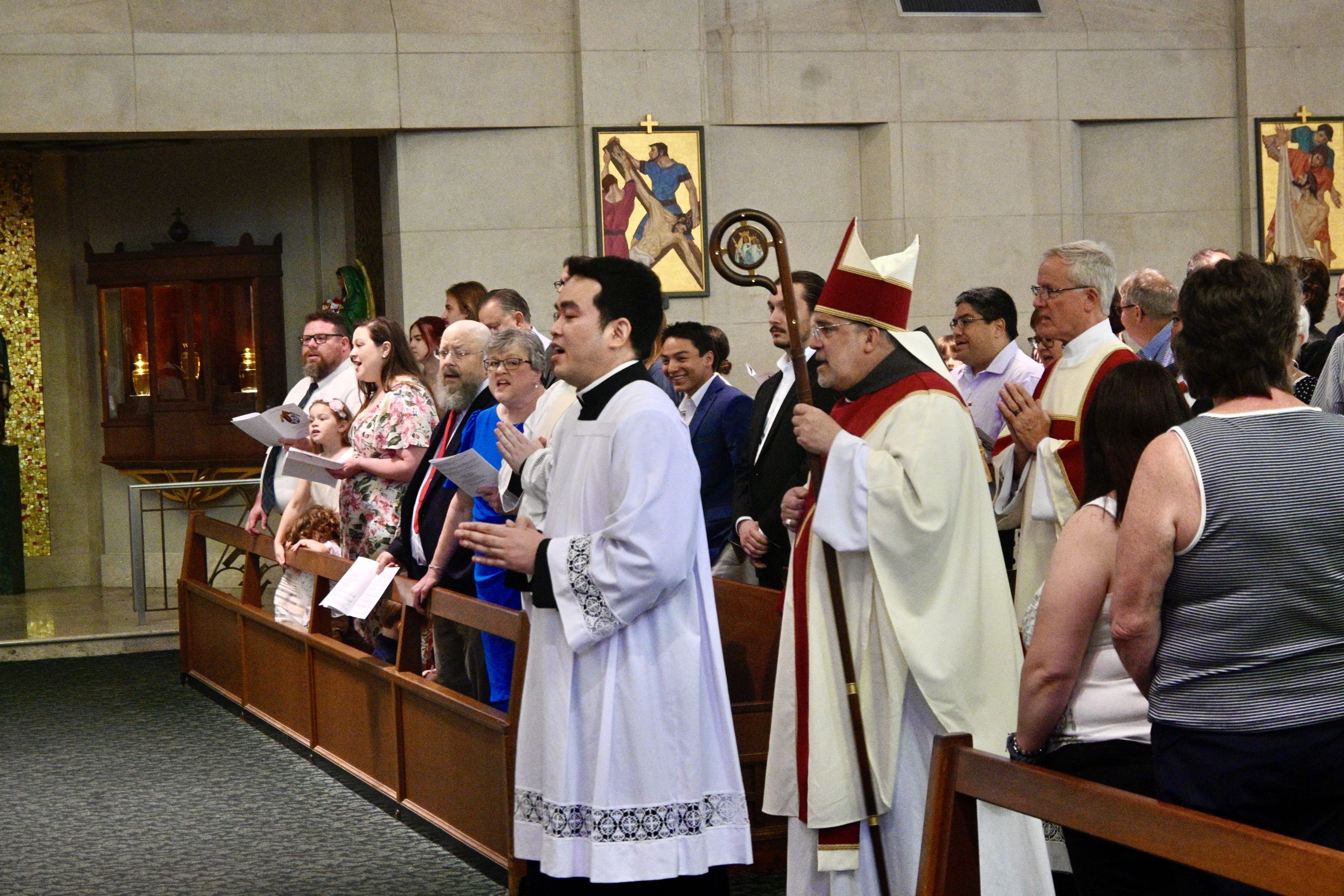 Group of clergy and parishioners standing in church pews, singing hymns during a liturgical service.